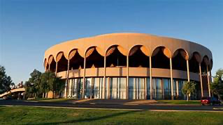 A circular building with arched windows with ASU Gammage in the background AI-generated content may be incorrect.